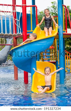 three little kids playing in the swimming pool on the slide
