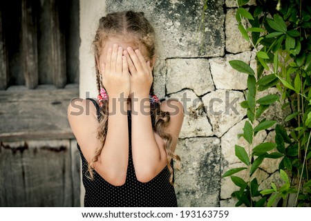 Portrait of sad little girl standing near stone wall at the day time