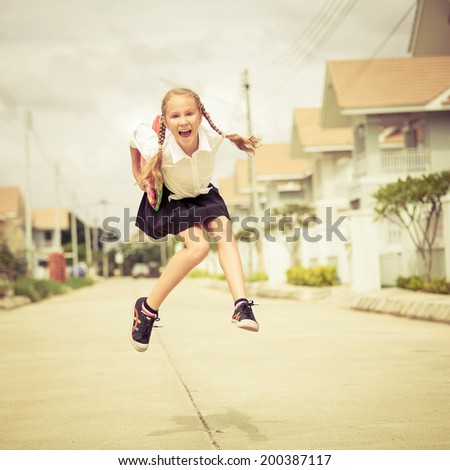 happy schoolgirl jumping near the house at the day time and ready to go to school