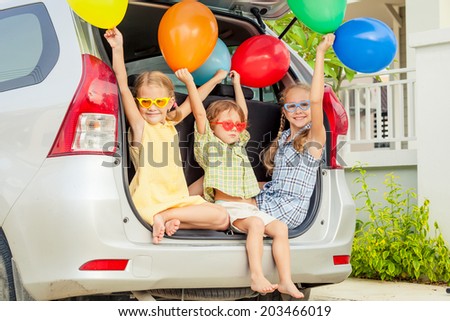 Brother and sisters with balloons sitting in the car near house at the day time