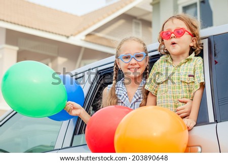 Brother and sister with balloons sitting in the car near window at the day time