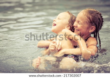 brother and sister playing in the swimming pool at the day time