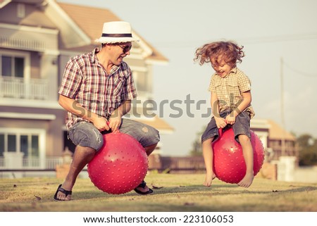 Dad and son jumping on inflatable balls on the lawn in front of house at the day time