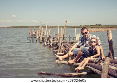 Father and son resting on the bridge in the sea at the day time. Concept of friendly family.