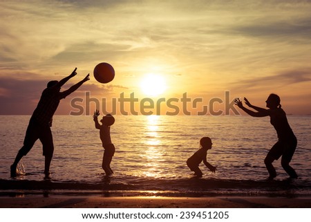 Silhouette of happy family who playing with the ball on the beach at the sunset time. Concept of friendly family.