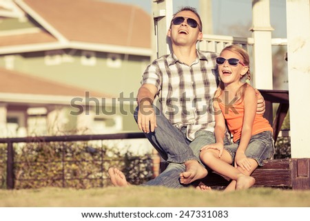 Father and daughter playing near the house at the day time. They sit in the white gazebo. Concept of friendly family.