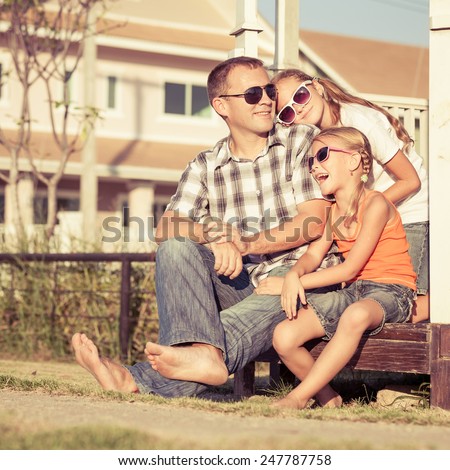 Father and daughters playing near the house at the day time. They sit in the white gazebo. Concept of friendly family.
