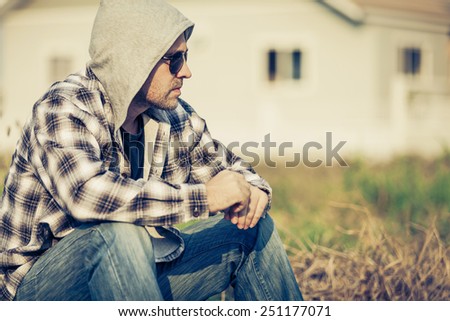 Portrait of a one sad man in sunglasses sitting outdoors near the house at the day time