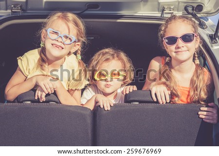 Happy brother and his two sisters are sitting in the car at the day time