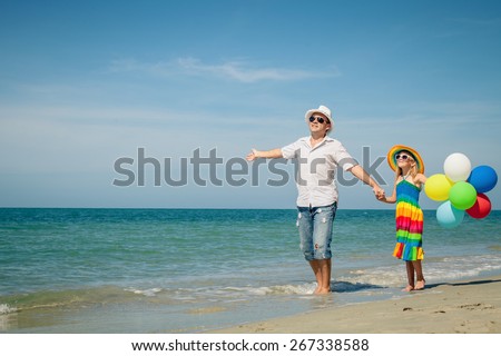 Father and daughter with balloons playing on the beach at the day time. Concept of friendly family.