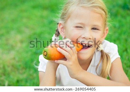 Happy little girl eating carrot at the day time. Concept of healthy food.