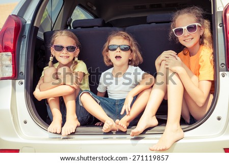 Happy brother and his two sisters are sitting in the car at the day time