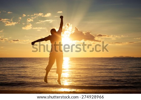 Man with his hands up at the sunset time on the beach