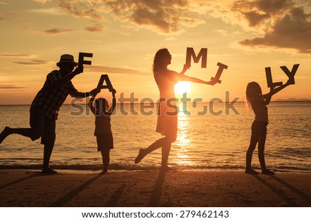 Happy family standing on the beach at the sunset time. They keep the letters forming the word \