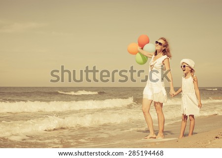 Mother and daughter playing with balloons on the beach at the day time. Concept of friendly family.