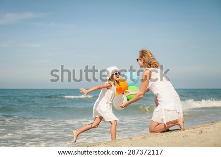 Mother and daughter playing with balloons on the beach at the day time. Concept of friendly family.