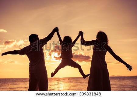 Silhouette of happy family who playing on the beach at the sunset time. Concept of friendly family.