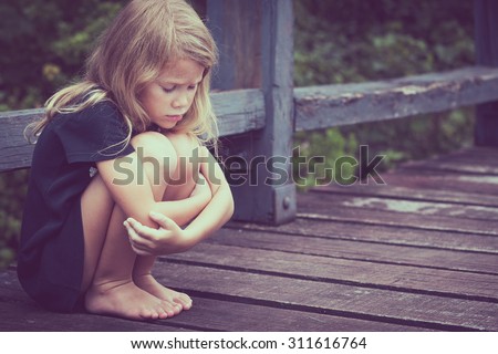 Portrait of sad blond little girl sitting on the bridge at the day time