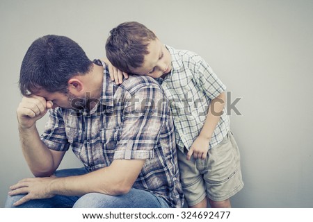 sad son hugging his dad near wall of house at the day time