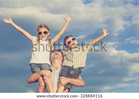 Father and children playing in the park  at the day time. Concept of friendly family. Picture made on the background of blue sky.