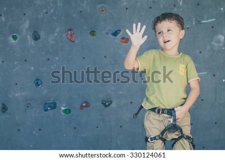 little boy standing near a rock wall for climbing indoor