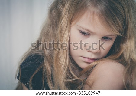 Portrait of sad little girl sitting near the window at home at the day time