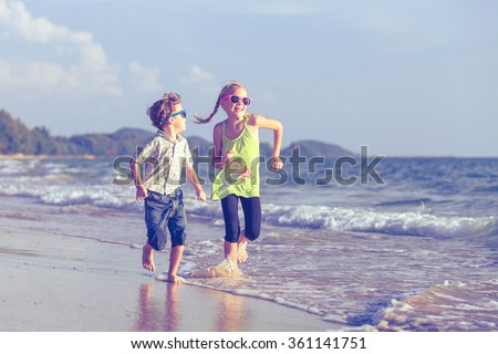 Happy children playing on the beach at the day time. Concept of happy friendly sister and brother.
