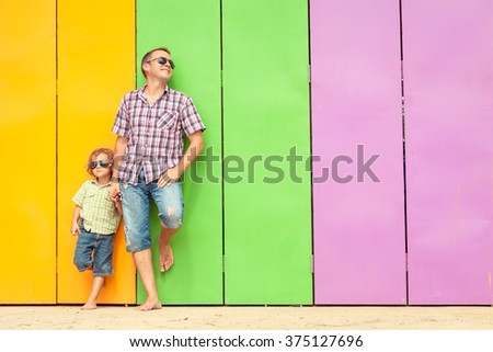 Father and son relaxing near the house at the day time. They standing near are the colorful wall. Concept of friendly family.