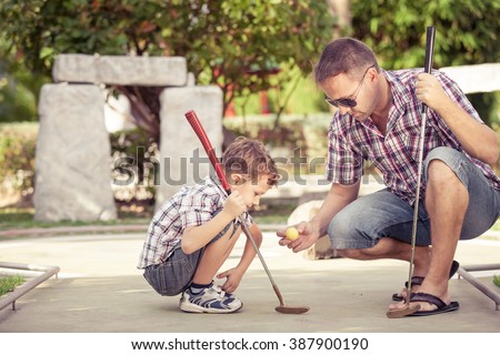 Sharing with golf experience. Cheerful young man teaching his son to play mini golf at the day time.  Concept of friendly family.