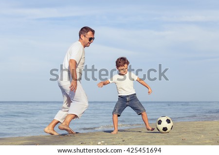 Father and son playing football on the beach at the day time. Concept of friendly family.