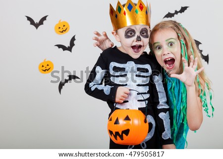 Happy brother and  sister on Halloween party. People having fun indoor. Children wearing costumes  skeletons and witches. Concept of children ready for a party.