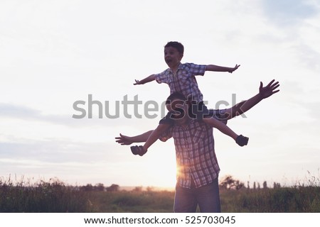 Father and son playing in the park at the sunset time. People having fun on the field. Concept of friendly family and of summer vacation.
