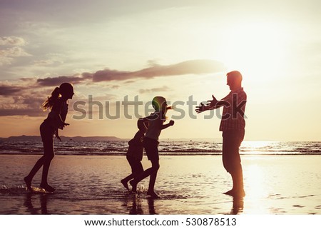 Father and children playing on the beach at the sunset time. Concept of friendly family.