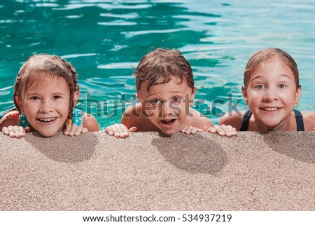 Three happy children playing on the swimming pool at the day time. People having fun outdoors. Concept of friendly siblings.