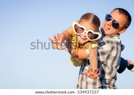 Dad and daughter in big sunglasses playing near a house at the day time. People having fun outdoors. Concept of friendly family.
