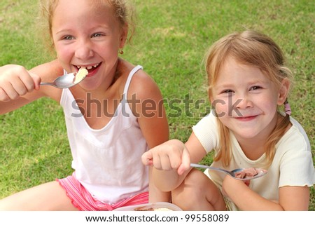 Two girls sitting on a green lawn and eat ice cream with a spoons