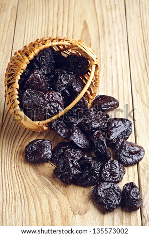 Dried plum in a basket and scattered on wooden table