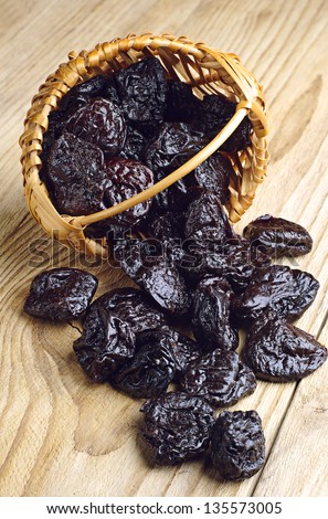Dried plum in a wicker basket and near on a wooden background