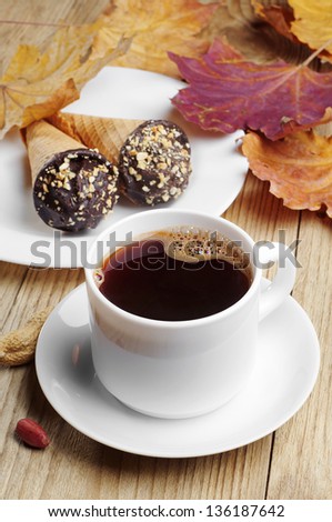 Cup of hot coffee with cakes in cream cone and maple autumn leaves