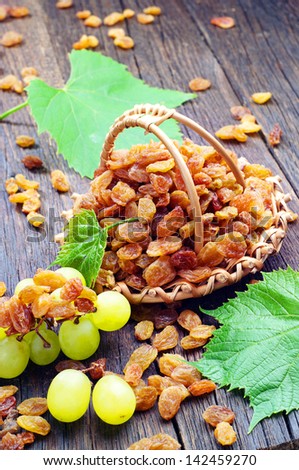 Raisin in a wicker basket, grapes and leaves on wooden table