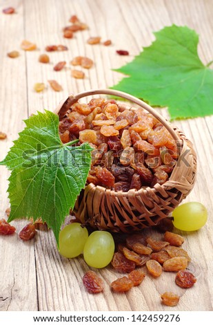 Raisin in a wicker basket and grapes with leaves on wooden table