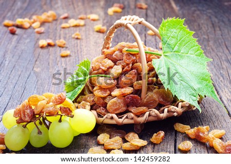 Raisin in a wicker basket and grapes on wooden table