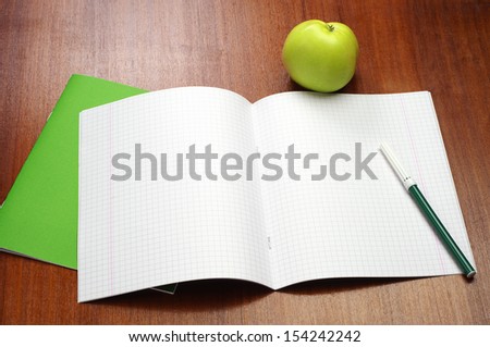 Opened school notebook, felt-tip pens and green apple on table