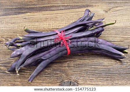Freshly harvested purple string beans tied with red ribbon on wooden table