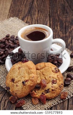 Cup of coffee and cookies with raisins and coffee beans on old wooden table