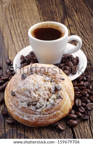 Cup of coffee, sweet bun and coffee beans on wooden table