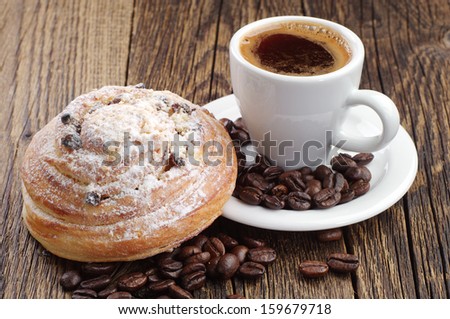 Cup of coffee, bun and coffee beans on wooden table