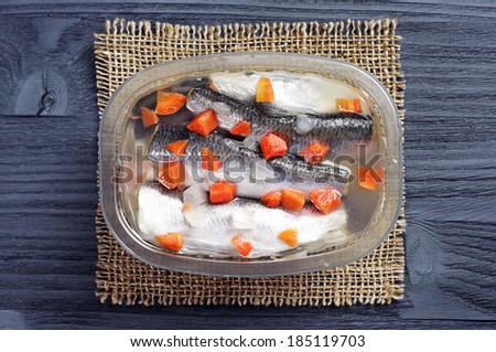 Marinated fish with carrots in jar on dark wooden background