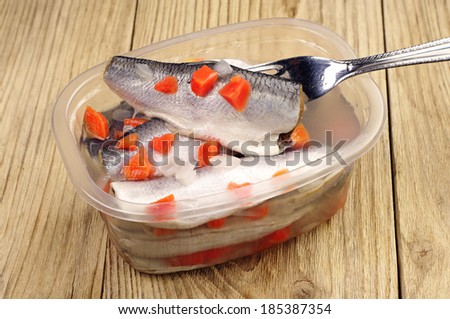 Marinated fish on a fork and in plastic jar on wooden background