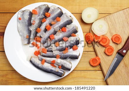 Marinated fish with carrots in a plate on wooden table. Top view